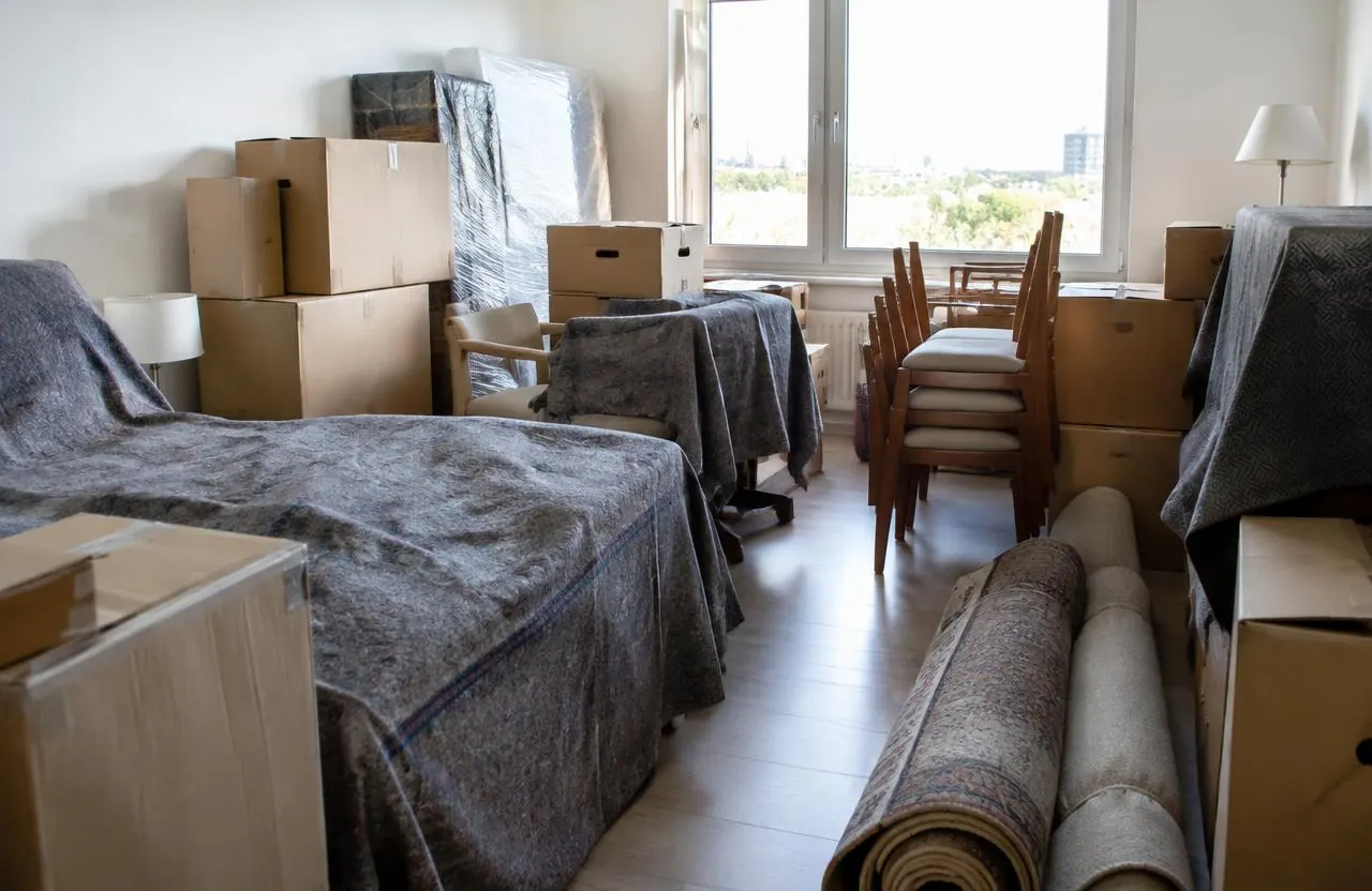 Zimmer voller Kartons und abgedeckter Möbel vor der Wohnungsauflösung
